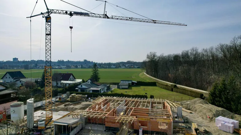 Baustelle eines Neubaus mit Kran und Rohbau in ländlicher Umgebung unter blauem Himmel.