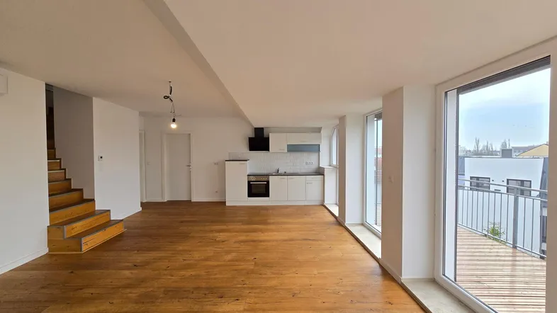 Heller offener Wohnbereich mit Holzboden, integrierter Küche und Zugang zu einem Balkon.