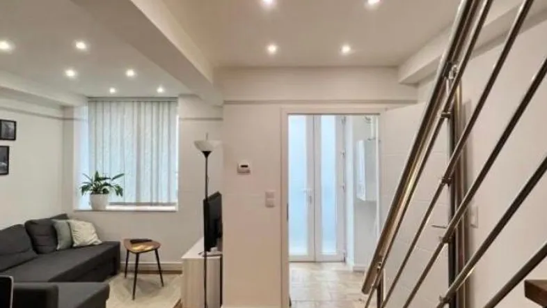 Helles Wohnzimmer mit Holzboden, moderner Einrichtung und offener Treppe zum Obergeschoss.