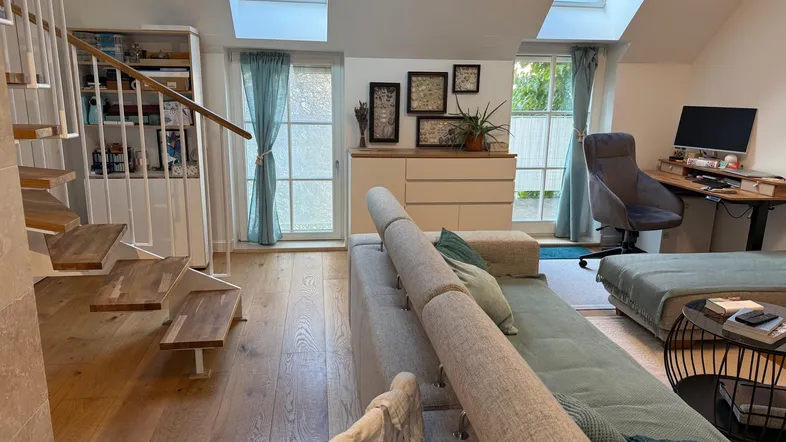 Helles Wohnzimmer mit Dachfenstern, Holztreppe und Zugang zu einem Balkon.