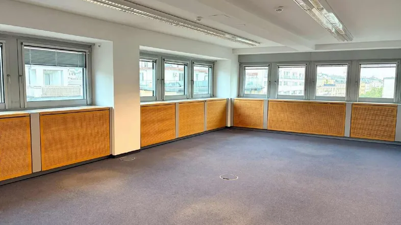 Geräumiges Büro mit Teppichboden, vielen Fenstern und Holzverkleidungen unter den Fensterbänken.