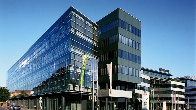 Modernes Bürogebäude mit großer Glasfassade und dunklen Paneelen unter blauem Himmel.