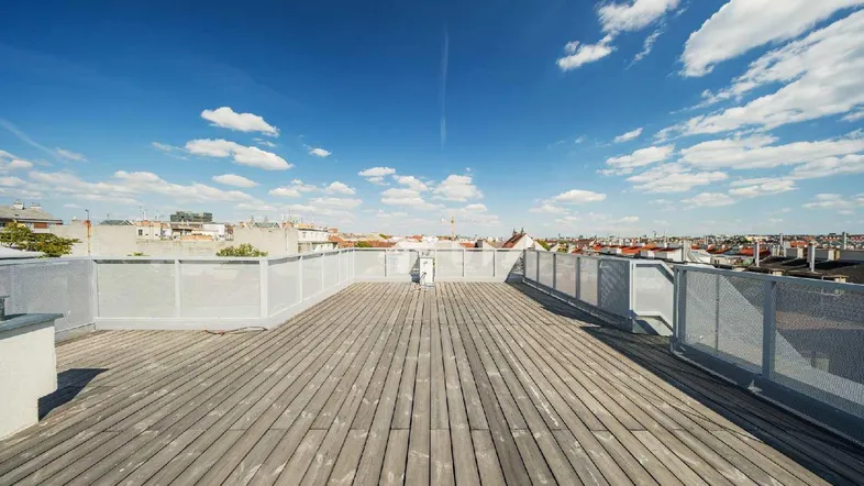 Große Dachterrasse mit Holzbelag und weitem Blick über die Stadt unter blauem Himmel.