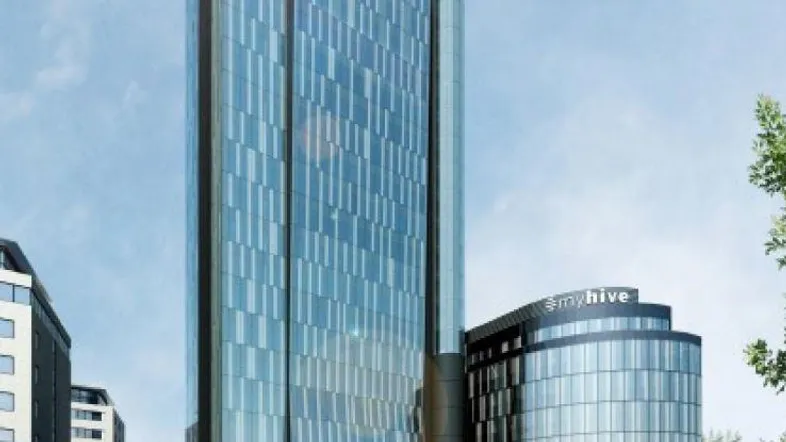 Hohes modernes Gebäude mit blauer Glasfassade und angrenzendem niedrigerem Bau unter klarem Himmel.