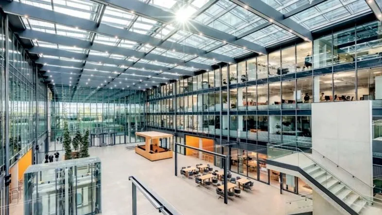 Großzügiges, modernes Büroatrium mit viel Tageslicht, Glasdach und mehreren Etagen, das eine offene und helle Atmosphäre schafft.