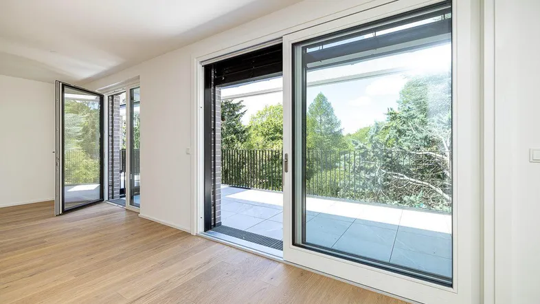 Heller Wohnraum mit Holzboden und großen Schiebetüren, die auf eine Terrasse mit Grünblick führen.