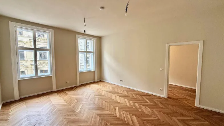 Geräumiges Wohnzimmer mit Fischgrätparkett und hohen Fenstern, bereit für die Einrichtung.