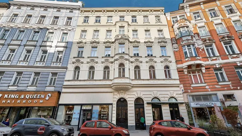 Klassisches Wiener Wohnhaus mit reich verzierter Fassade und Geschäften im Erdgeschoss an einer belebten Straße.