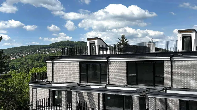 Modernes Gebäude mit Ziegelfassade, mehreren Balkonen und einer Dachterrasse mit weitem Blick ins Grüne.