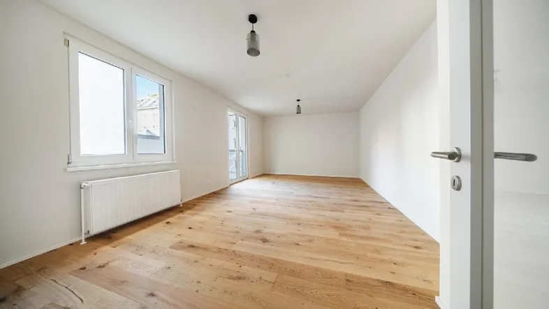 Helles, leeres Zimmer mit neuem Parkettboden, großen Fenstern und Zugang zu einem Balkon.