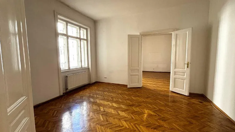 Helles Zimmer mit Fischgrätparkett und hohen Doppeltüren, das viel Tageslicht hereinlässt.