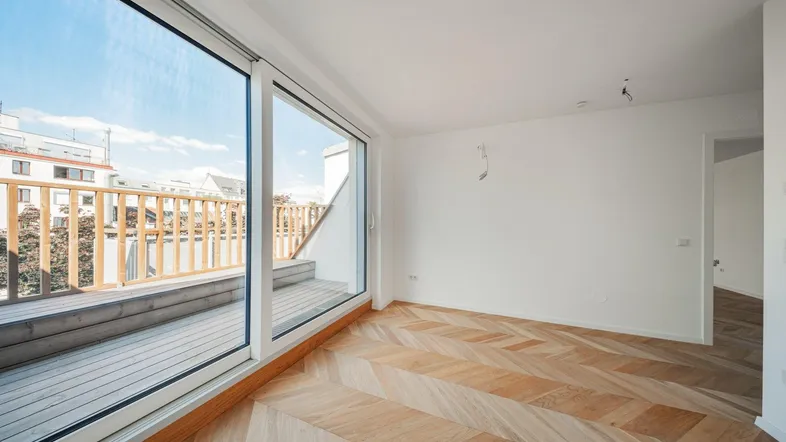 Helles Zimmer mit Fischgrätparkett und Zugang zu einer Holzterrasse, ideal für Wohn- oder Schlafbereich.