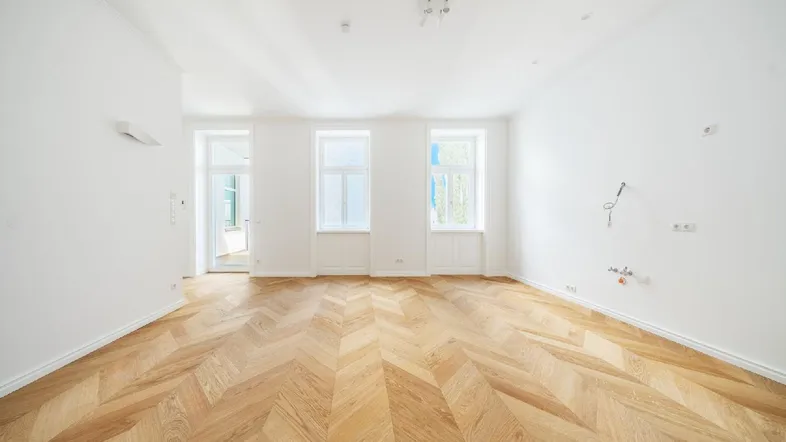 Helles, leeres Zimmer mit Fischgrätparkett und hohen Fenstern, bereit zur individuellen Gestaltung.