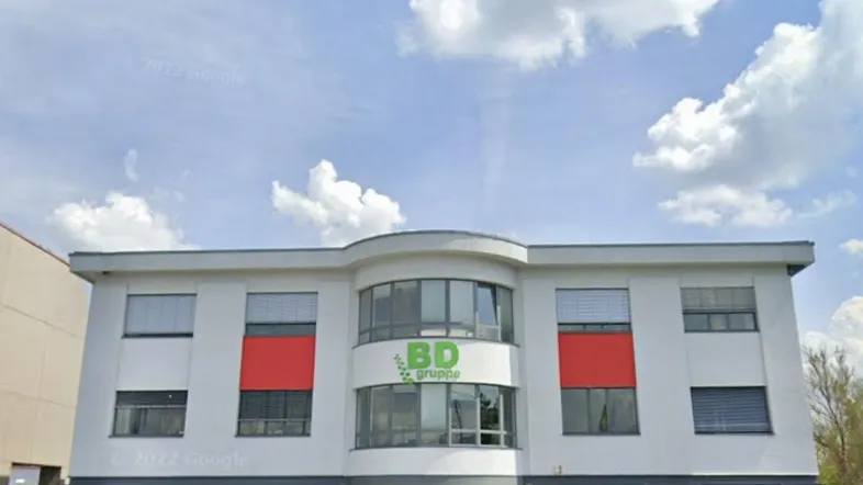 Modernes Bürogebäude mit großen Fenstern und roten Akzenten unter blauem Himmel.