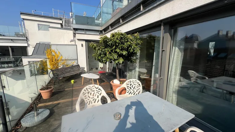 Sonnige Dachterrasse mit Holzboden, Glasgeländer und Sitzgelegenheiten, ideal zum Entspannen im Freien.