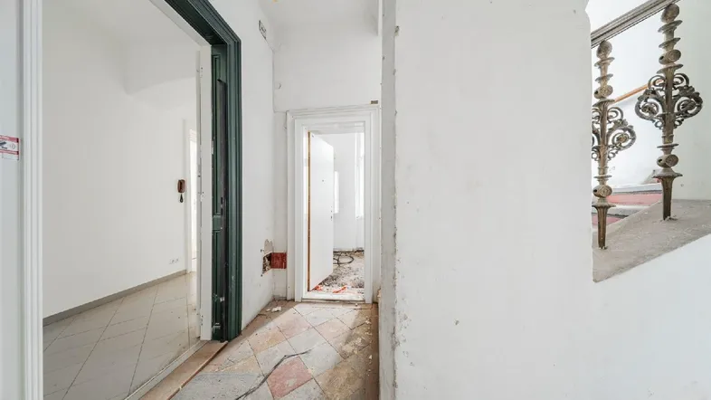 Langer Flur mit Fliesenboden, grünen Türrahmen und Zugang zu weiteren Räumen im Altbau.