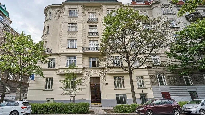 Klassische Fassade eines Mehrfamilienhauses mit dekorativen Elementen, Balkonen und Bäumen davor.