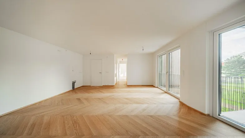 Geräumiges, helles Zimmer mit modernem Fischgrätparkett und Zugang zu einem Balkon.