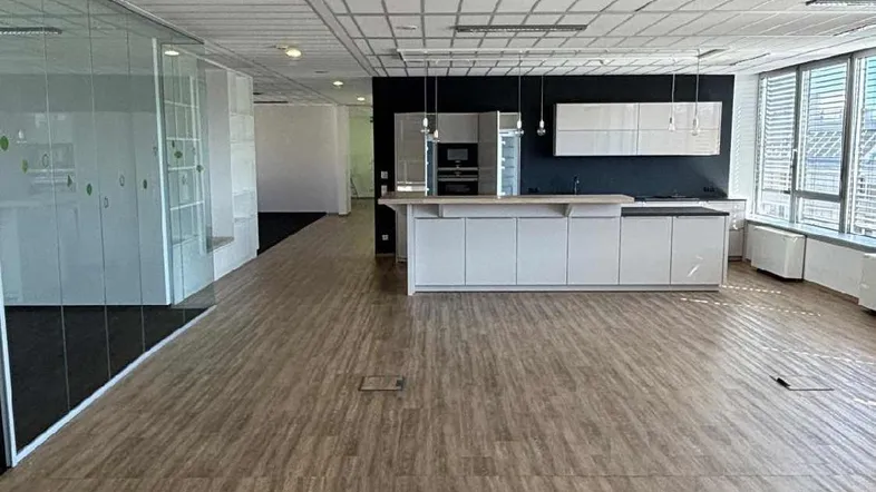 Modernes Großraumbüro mit integrierter Küchenzeile, Holzboden und großen Fenstern für viel Tageslicht.