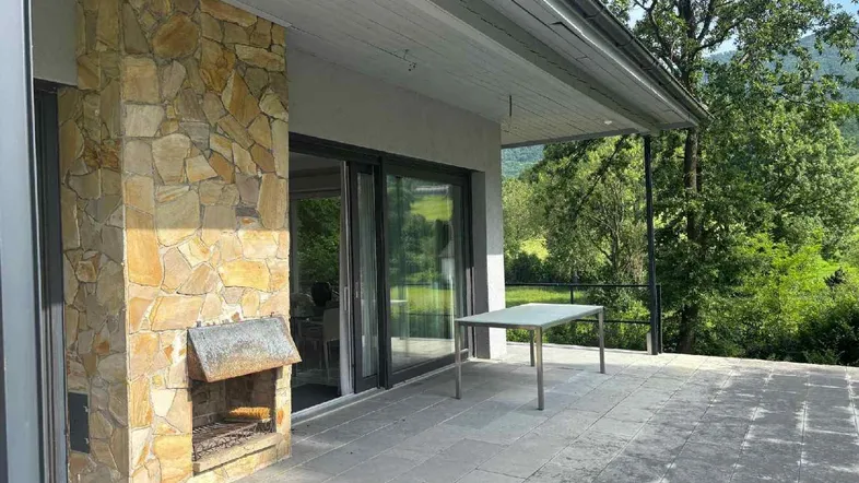 Große Steinterrasse mit integriertem Grill und Blick auf die umliegende grüne Landschaft.