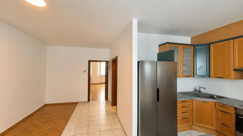 Küche mit Holzschränken, Granitarbeitsplatte und großem Kühlschrank, angrenzend an einen Flur.