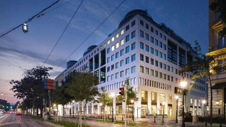 Moderne Geschäftsgebäude-Fassade bei Dämmerung mit beleuchteten Fenstern und Straßenbahnlinien in der Stadt.