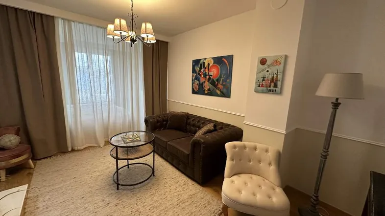 Helles Wohnzimmer mit beigem Teppich, braunem Sofa, Stehlampe und dekorativen Kunstwerken.