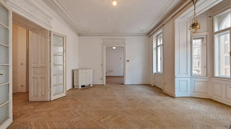 Geräumiges Wohnzimmer mit Fischgrätparkett, hohen Decken und Stuckverzierungen, bereit zur Renovierung.
