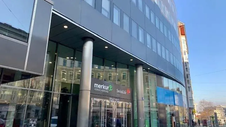 Moderne Bürogebäude-Fassade mit großen Glasflächen und Firmenlogos am Eingangsbereich.