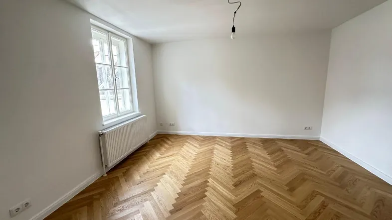 Helles Zimmer mit Fischgrätparkettboden, weißen Wänden und einem Fenster, bereit zur Einrichtung.