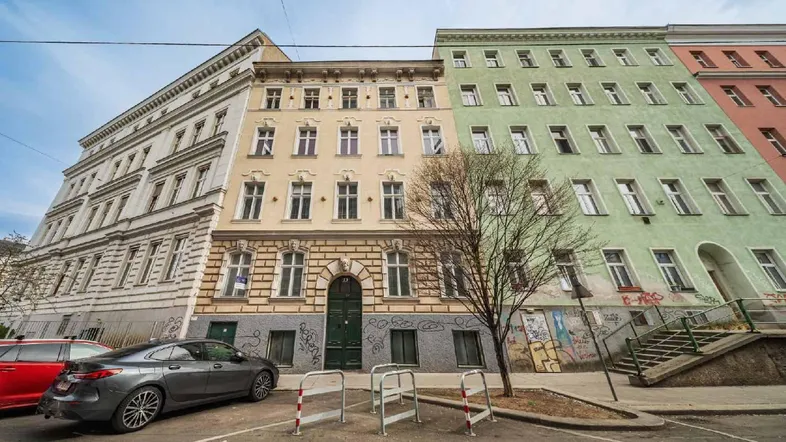 Mehrere Altbaugebäude mit unterschiedlichen Fassadenfarben und parkenden Autos auf der Straße.