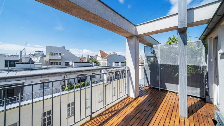 Geräumige Dachterrasse mit Holzboden und Blick über die Dächer der Stadt an einem sonnigen Tag.