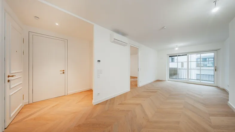 Helles, modernes Wohnzimmer mit Fischgrätparkett und Zugang zu einem Balkon.