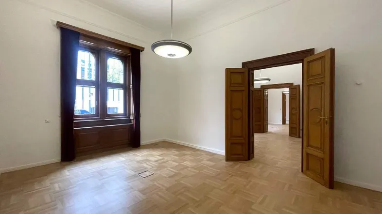 Geräumiger Innenraum mit Fischgrätparkett, hohen Decken und großen Holzfenstern, die viel Tageslicht hereinlassen.