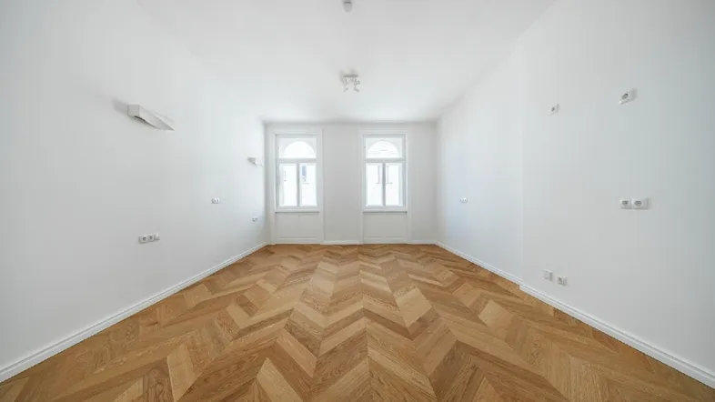 Helles, leeres Zimmer mit Fischgrätparkett und hohen Fenstern, bereit zur individuellen Gestaltung.