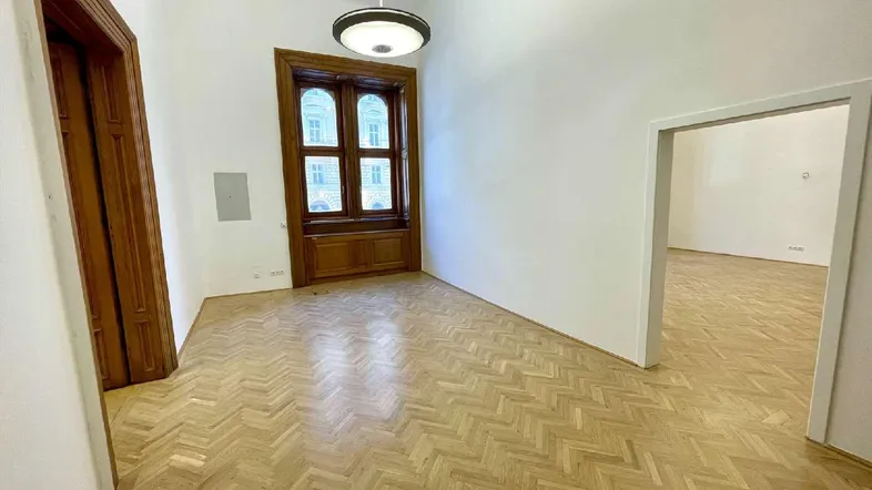 Geräumiger, leerer Raum mit Fischgrätparkett und hohen Fenstern, ideal für Büronutzung.