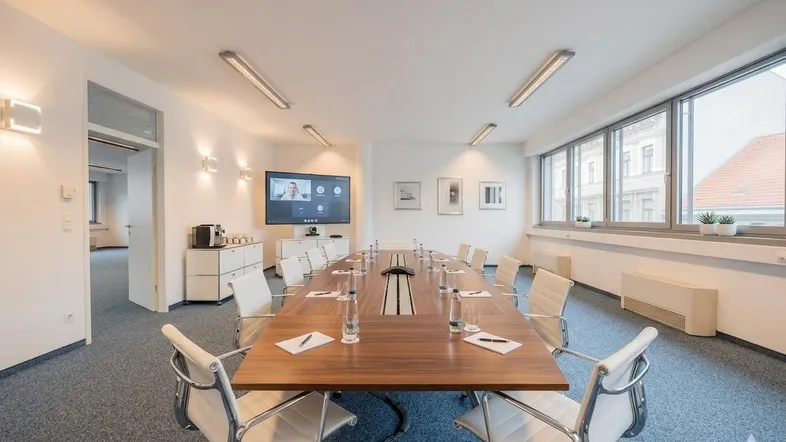 Moderner Konferenzraum mit großem Holztisch, bequemen Stühlen und Blick nach draußen.