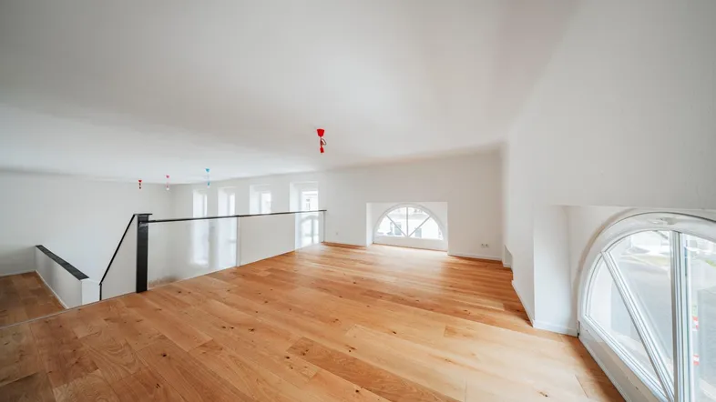 Großer, heller Raum mit Holzboden, hohen Decken und einer Galerie, ideal für vielseitige Nutzung.