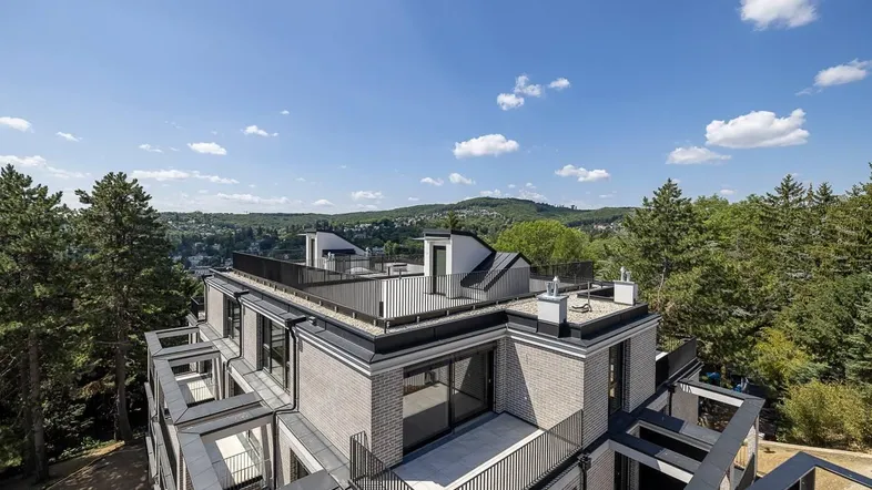 Luftaufnahme eines modernen Gebäudekomplexes mit Flachdach, Terrassen und grüner Umgebung.