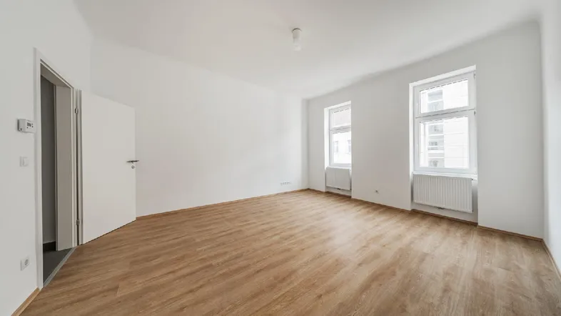 Helles, leeres Zimmer mit neuem Laminatboden und weißen Wänden, bereit zur Einrichtung.