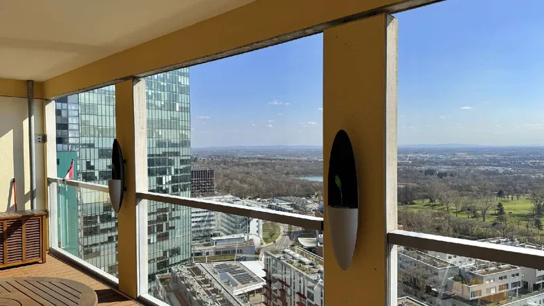 Heller Balkon mit Holzboden und Panoramablick auf die Stadt und umliegende Natur.