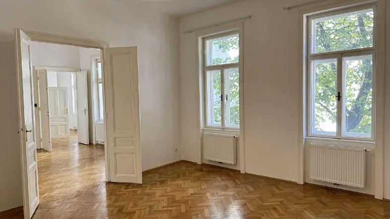 Helles Zimmer mit Fischgrätparkettboden und hohen Fenstern, das viel Tageslicht hereinlässt.