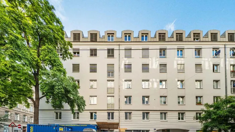Fassade eines modernen Wohngebäudes mit vielen Fenstern und Mansarddach in städtischer Umgebung.