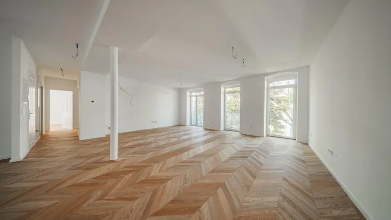 Geräumiges, helles Zimmer mit Fischgrätparkett, weißen Wänden und Zugang zu französischen Balkonen.