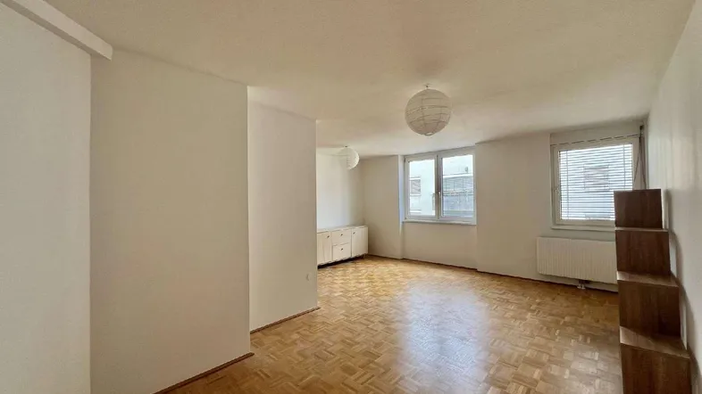 Helles Zimmer mit Parkettboden, weißen Wänden und zwei Fenstern, bereit zur individuellen Gestaltung.