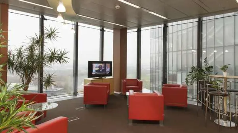 Moderner Loungebereich mit roten Sesseln, Fernseher und großen Fenstern mit Stadtblick.