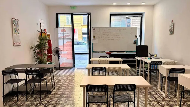 Heller und geräumiger Klassenraum mit mehreren Tischen, Stühlen und einer großen Whiteboard-Tafel.