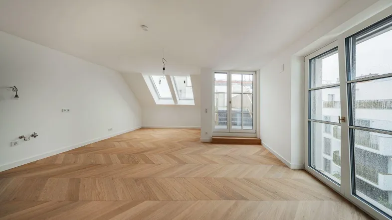 Helles Zimmer mit Fischgrätparkett, Dachschrägen und Zugang zu einem französischen Balkon.