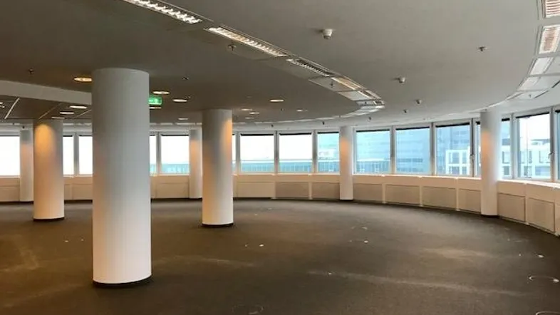 Großer, offener Büroraum mit Teppichboden, vielen Fenstern und Säulen, bereit für die Gestaltung.