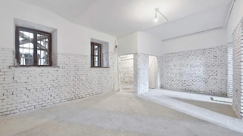 Heller Lagerraum mit weiß gestrichenen Ziegelwänden, Betonboden und zwei Fenstern für Tageslicht.